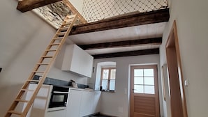 A kitchen with white cabinets, a wooden ladder, a stone wall, and a door. - Apartment Stadtmauerloft Gmünd by Interhome (Fischertratten)