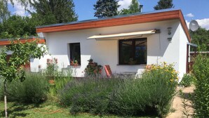 A modern house with a white exterior and a red roof, surrounded by a well-maintained garden with various plants and flowers. - Kleines Ferienhaus in Rangsdorf mit großem Garten by Interhome (Rangsdorf)