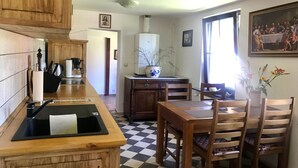 A kitchen with wooden cabinets, a black countertop, and a checkered floor. There is a dining table with chairs and a potted plant on the windowsill. - Kleines Ferienhaus in Rangsdorf mit großem Garten by Interhome (Rangsdorf)