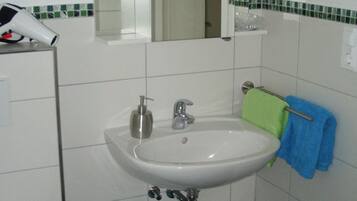 A bathroom with a white sink, a mirror above it, a toilet, a trash bin, and a blue mat on the floor.