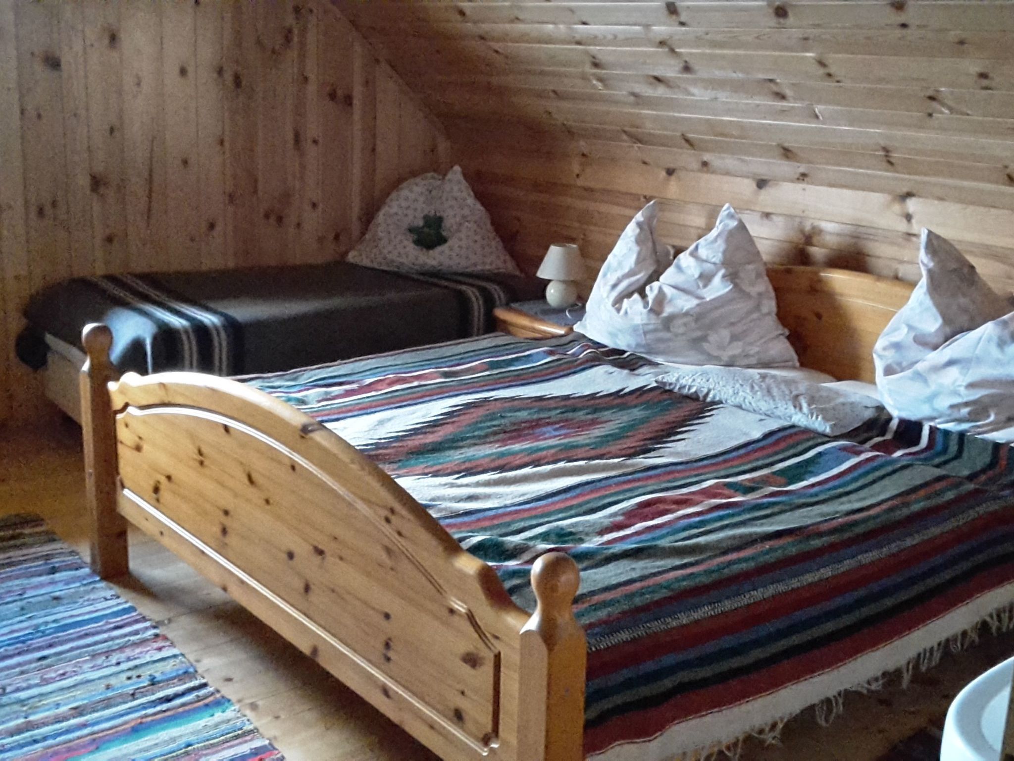Een houten bed met een gestreept dekbed en kussens in een kamer met houten wanden.