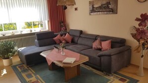 A modern living room with a grey sectional sofa, a small coffee table, a potted plant, and a large window with curtains. - Appartement mit Terrasse, Garten und Grill by Interhome (Böbrach)