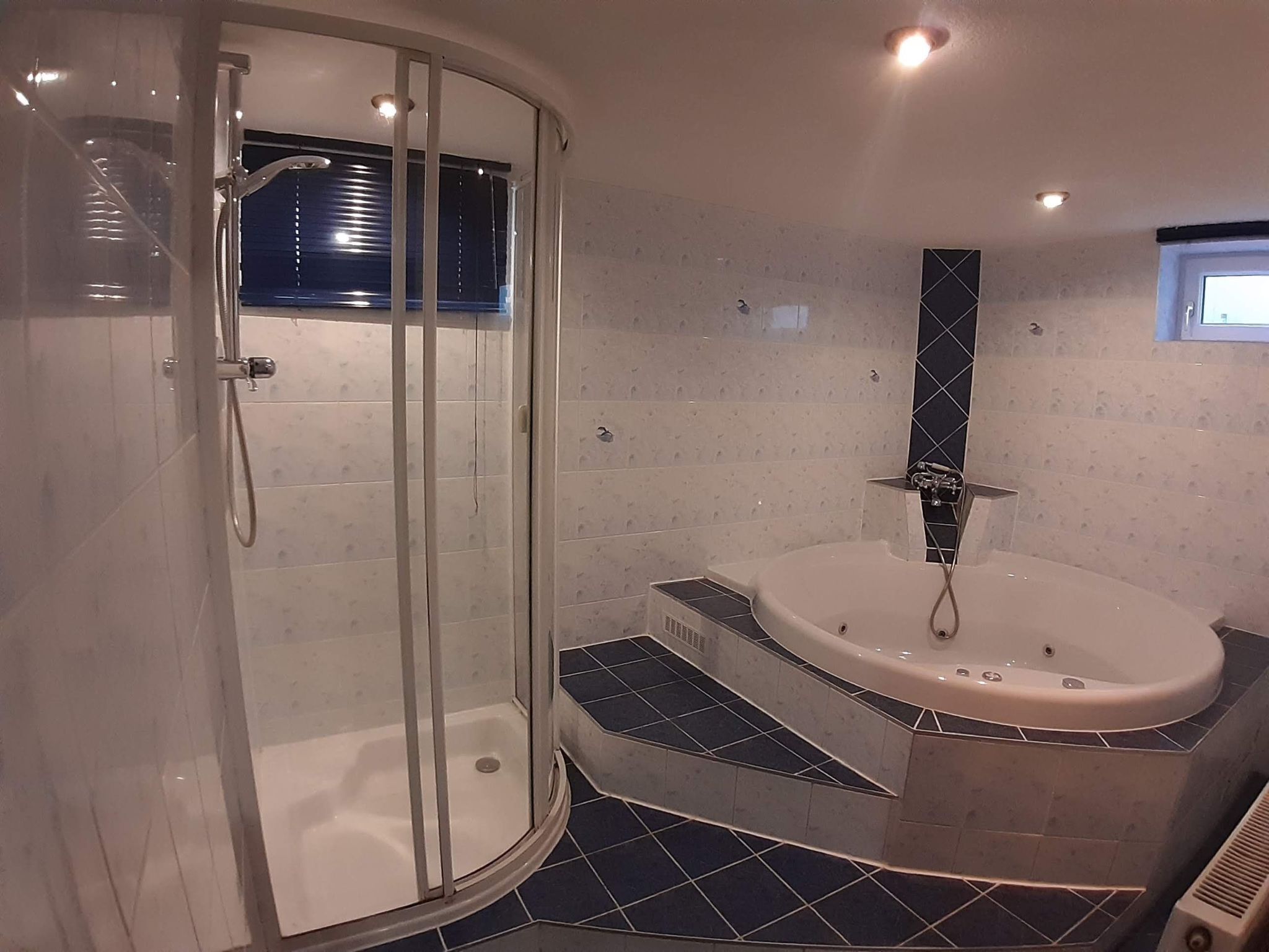 A modern bathroom with a glass-enclosed shower, a freestanding bathtub, and a small window.