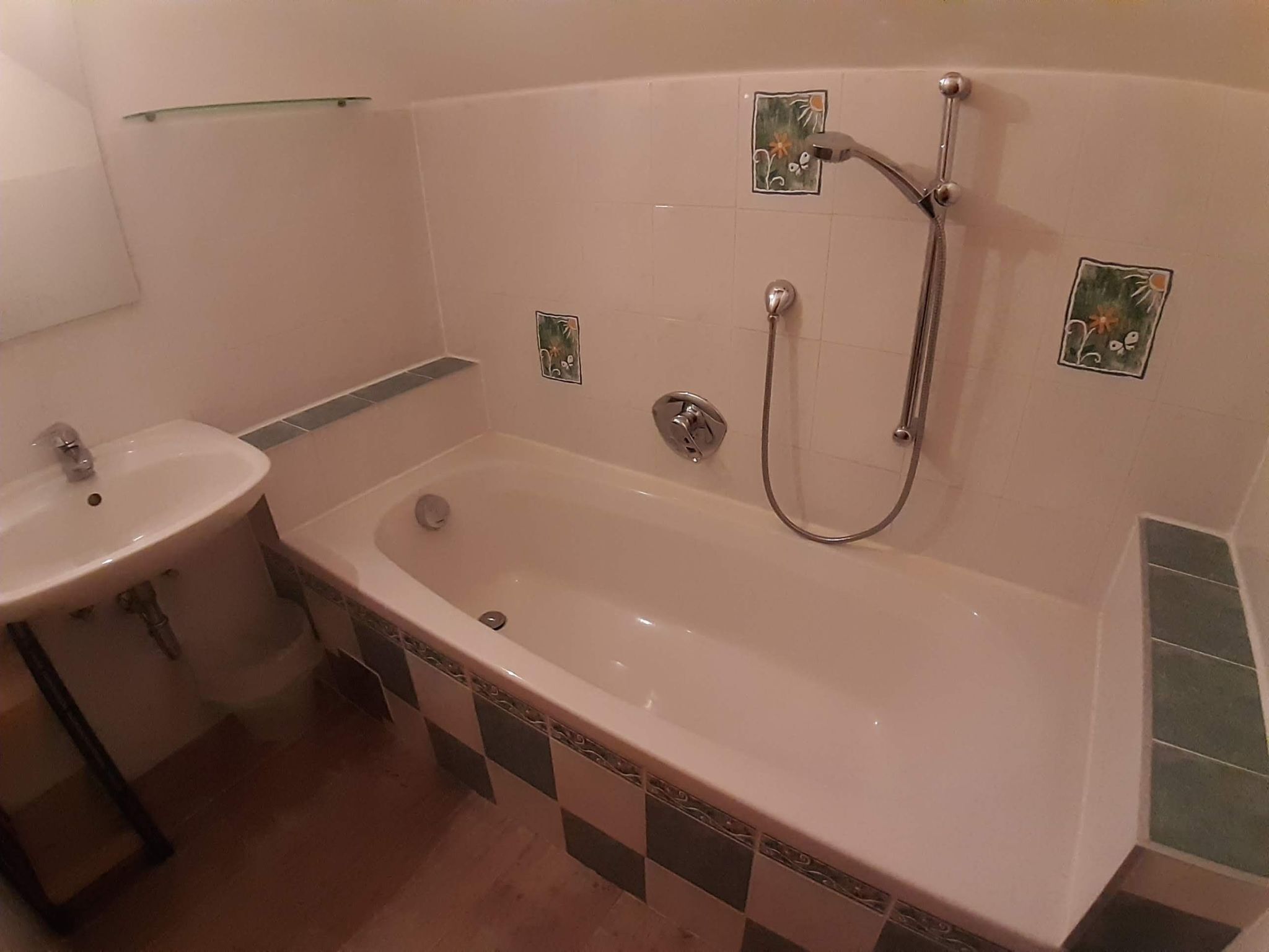A bathroom with a bathtub, a sink, and decorative tiles.