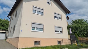Ein mehrstöckiges Wohngebäude mit beiger Fassade, mehreren Fenstern mit Fensterläden und einer Satellitenschüssel.