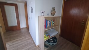 Ein Flur mit Holzboden, einer Bücherwand mit Büchern und Dekoration, einem Haustierbett und einer Tür mit mattiertem Glas.