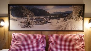 A bed with red and white checkered pillows, a framed landscape picture above, and wooden paneling on the wall. - Sonnenhof by Interhome (Umhausen)