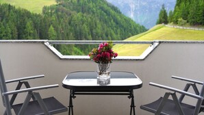 A balcony with a table and two chairs, a vase with flowers, and a scenic mountain view. - Sonnenhof by Interhome (Umhausen)