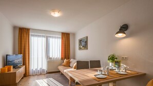 Een moderne woonkamer met een bank, een eettafel gedekt met borden en glazen, een televisie en een schilderij aan de muur.