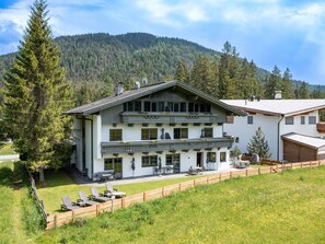 Ein zweistöckiges Gebäude mit Balkon, umgeben von einem Holzzaun und einer Rasenfläche mit Außenbestuhlung.