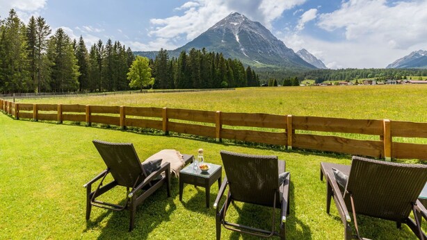 Un espacio al aire libre con asientos de mimbre y una mesa, con vistas a una montaña y un valle boscoso.