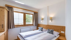 Una cama doble con sábanas blancas, un cabecero de madera, una ventana con cortinas y dos lámparas fijadas a la pared.