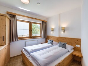 Ein Doppelbett mit weißen Bettwäsche, ein Holz-Kopfteil, ein Fenster mit Vorhängen und zwei Wandleuchten.