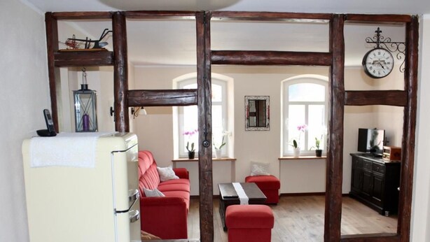Un salon chaleureux avec un canapé rouge, une table basse en bois et un réfrigérateur blanc.
