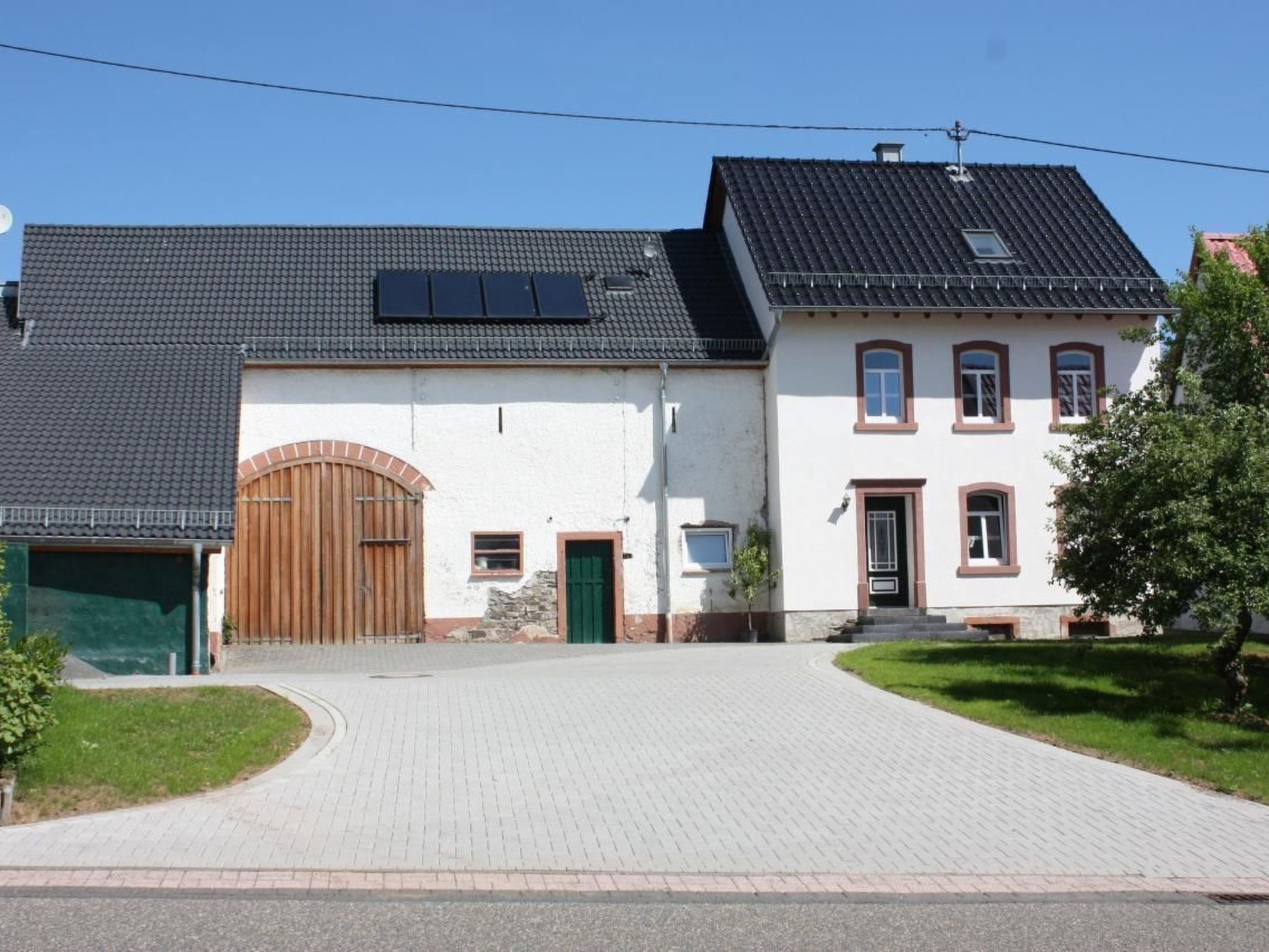 Ein zweistöckiges Haus mit gepflasterter Auffahrt, einer Holztür zur Garage und einem kleinen Garten.
