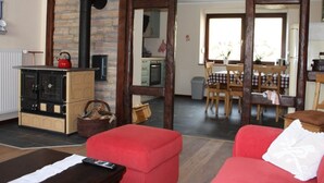 Un salon chaleureux avec un canapé rouge, une cheminée et un coin repas comprenant une table et des chaises.
