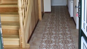Un couloir avec un escalier en bois, des carreaux de sol à motifs et une porte au fond.