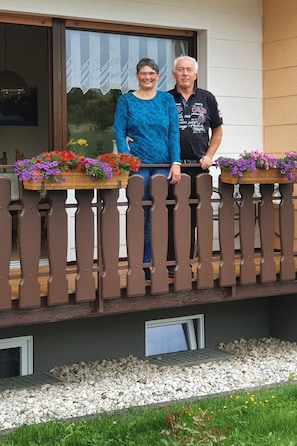 Een balkon met houten spijlen, een raam met uitzicht op groen en bloempotten.