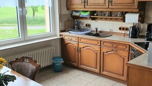 Ett kök med träskåp, ett fönster med gardiner, en diskho och ett matbord med stolar.