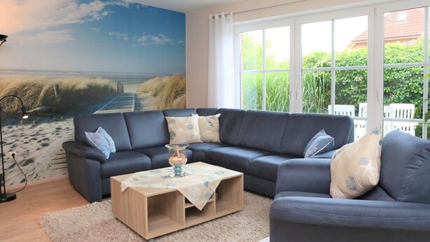 A living room with a large window, a dark blue sofa, a wooden coffee table, and a beach mural on the wall. - Martina 3 by Interhome (Friederikensiel)