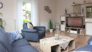 A modern living room with a sofa, coffee table, TV, and a window with curtains. - Martina 3 by Interhome (Friederikensiel)