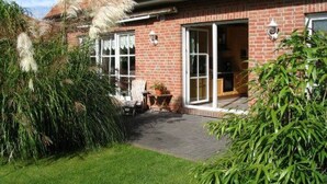 A brick house with a red-tiled roof, a front door, and a small patio area with a table and chairs. - Martina 3 by Interhome (Friederikensiel)
