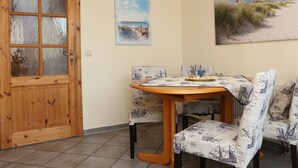 A dining area with a wooden table and patterned chairs, a wooden door, and maritime-themed wall art. - Martina 3 by Interhome (Friederikensiel)