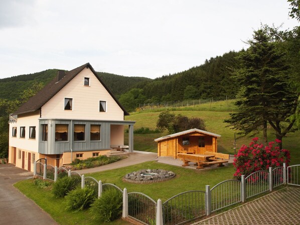 Ein zweistöckiges Haus mit überdachter Veranda und einer kleinen Holzhütte.