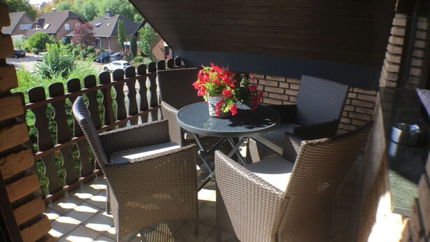 Un patio con mobiliario de mimbre, una mesa, valla de madera y vistas a casas al fondo.