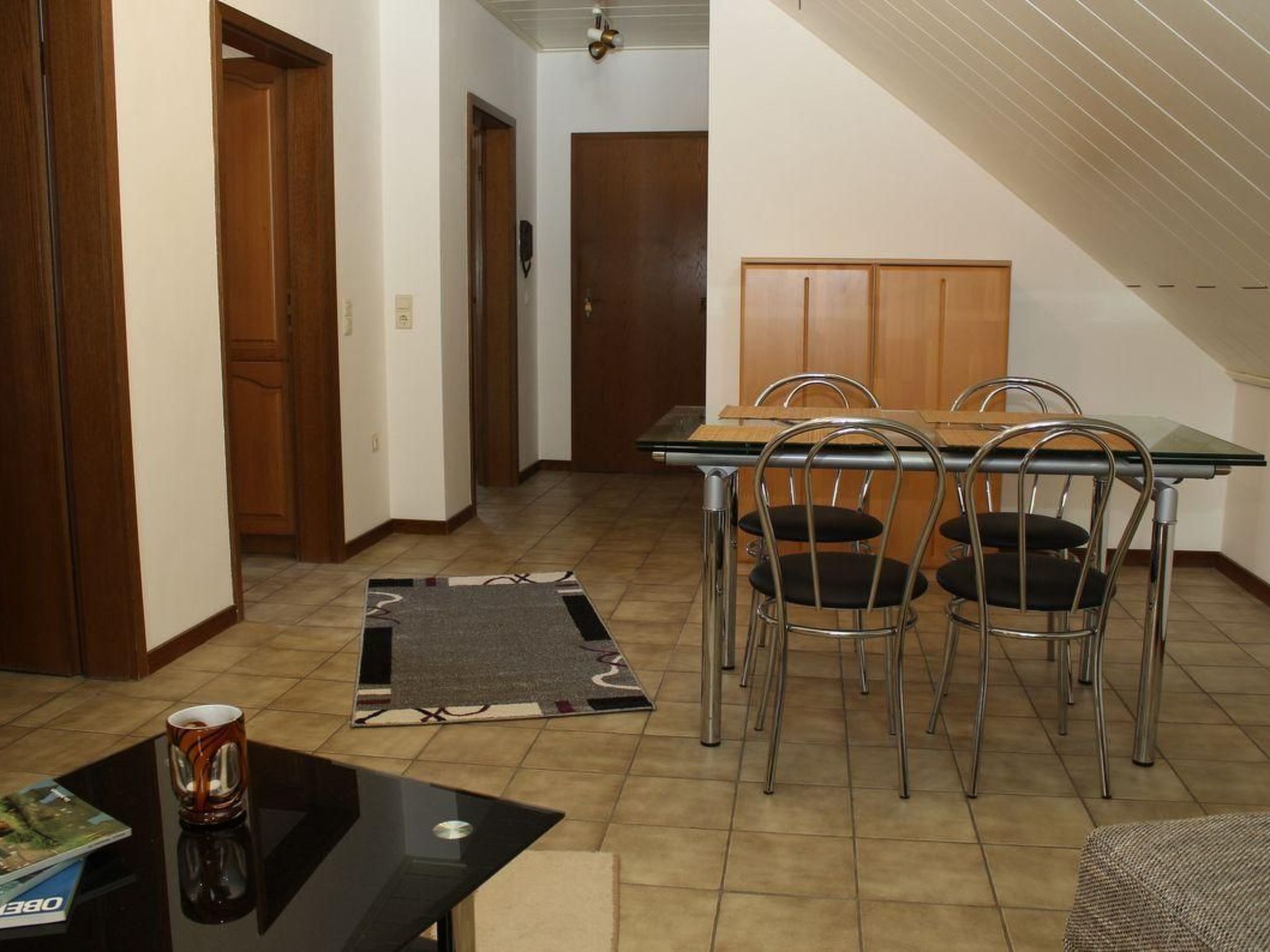 A dining area with a wooden table and four metal chairs, a black coffee table, and a magazine.