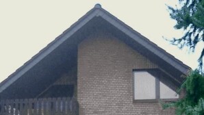 Un edificio de dos pisos con fachada de ladrillo, un balcón en el nivel superior y una ventana en el inferior.