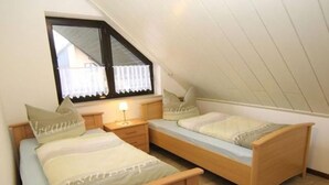 Una habitación pequeña y acogedora con dos camas de madera, una mesita de noche, una lámpara y una ventana con cortinas.