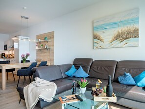 A modern living room with a sofa, coffee table, and a painting of a beach scene. - Apartment Kleine Auszeit by Seeblick Ferien ORO by Interhome (Hasselberg)