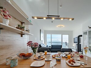 A modern kitchen with a dining table set for breakfast, a large window with a view, and a TV mounted on the wall. - Apartment Kleine Auszeit by Seeblick Ferien ORO by Interhome (Hasselberg)