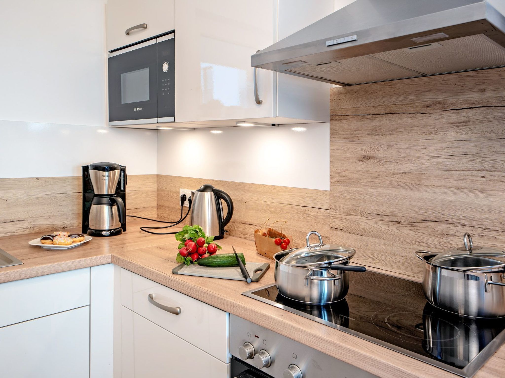 A modern kitchen with a microwave, coffee maker, kettle, and two pots on an induction cooktop.