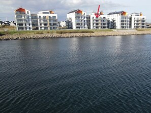 Un immeuble résidentiel situé au bord de l’eau, doté de nombreux balcons et offrant une vue sur le plan d’eau.