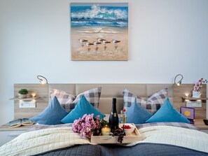 A bedroom with a bed, pillows, a bedside table with a lamp, a nightstand, and a painting of birds on the wall. - Apartment Kleine Auszeit by Seeblick Ferien ORO by Interhome (Hasselberg)