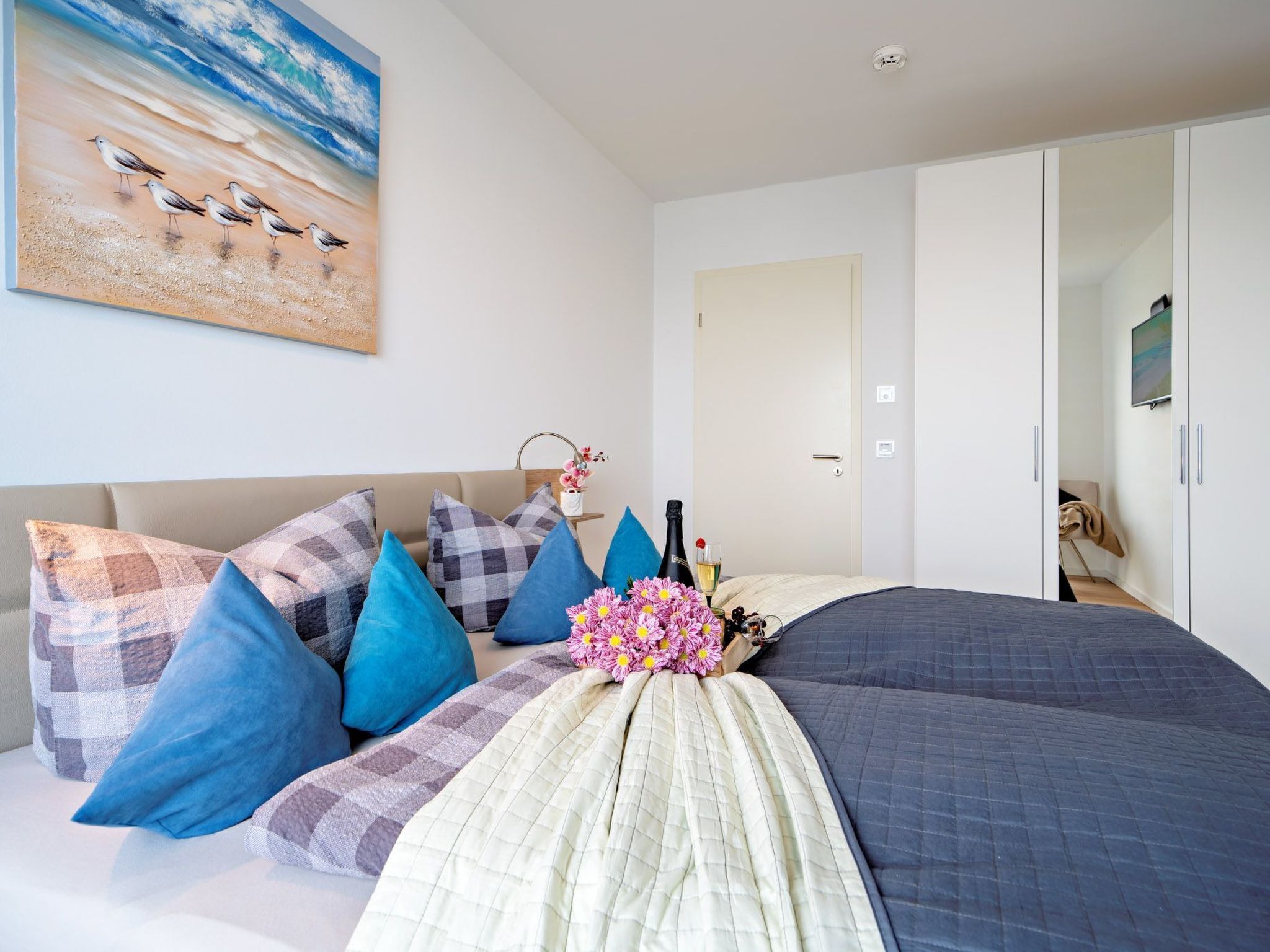 Ein Schlafzimmer mit einem Bett, Kissen, einem Gemälde, einer Flasche und einem Glas.