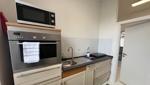 Cocina compacta con microondas, horno, lavamanos y una puerta que da a otra habitación.