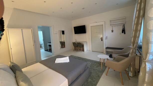 Habitación de hotel moderna con una cama grande, una zona de estar con una mesita pequeña, un televisor montado en la pared y una puerta que da a un baño.