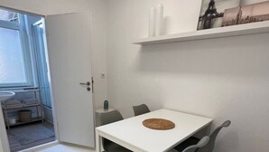 Un comedor moderno con una mesa blanca y sillas grises, un tapete azul oscuro y una puerta blanca que da a otra habitación.