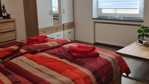 Ein Schlafzimmer mit Bett, Schrank, Heizkörper, Fenster mit Jalousien und einem kleinen Tisch mit Pflanze.