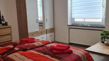 A bedroom with a bed, a wardrobe, a radiator, a window with blinds, and a small table with a plant.
