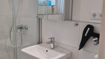 Ein modernes Badezimmer mit einer Duschkabine aus Glas, einem weißen Waschbecken und einem Spiegel darüber.