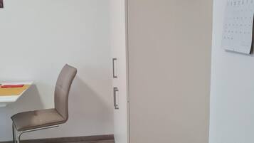 Et værelse med en beige garderobe, et skrivebord med stol, en skraldespand og en kalender på væggen.