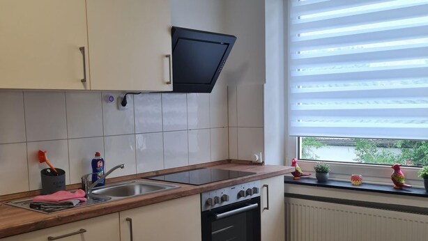 Eine Küche mit weißen Schränken, einem eingebauten Backofen, einer Spüle und einem Fenster mit Jalousien.