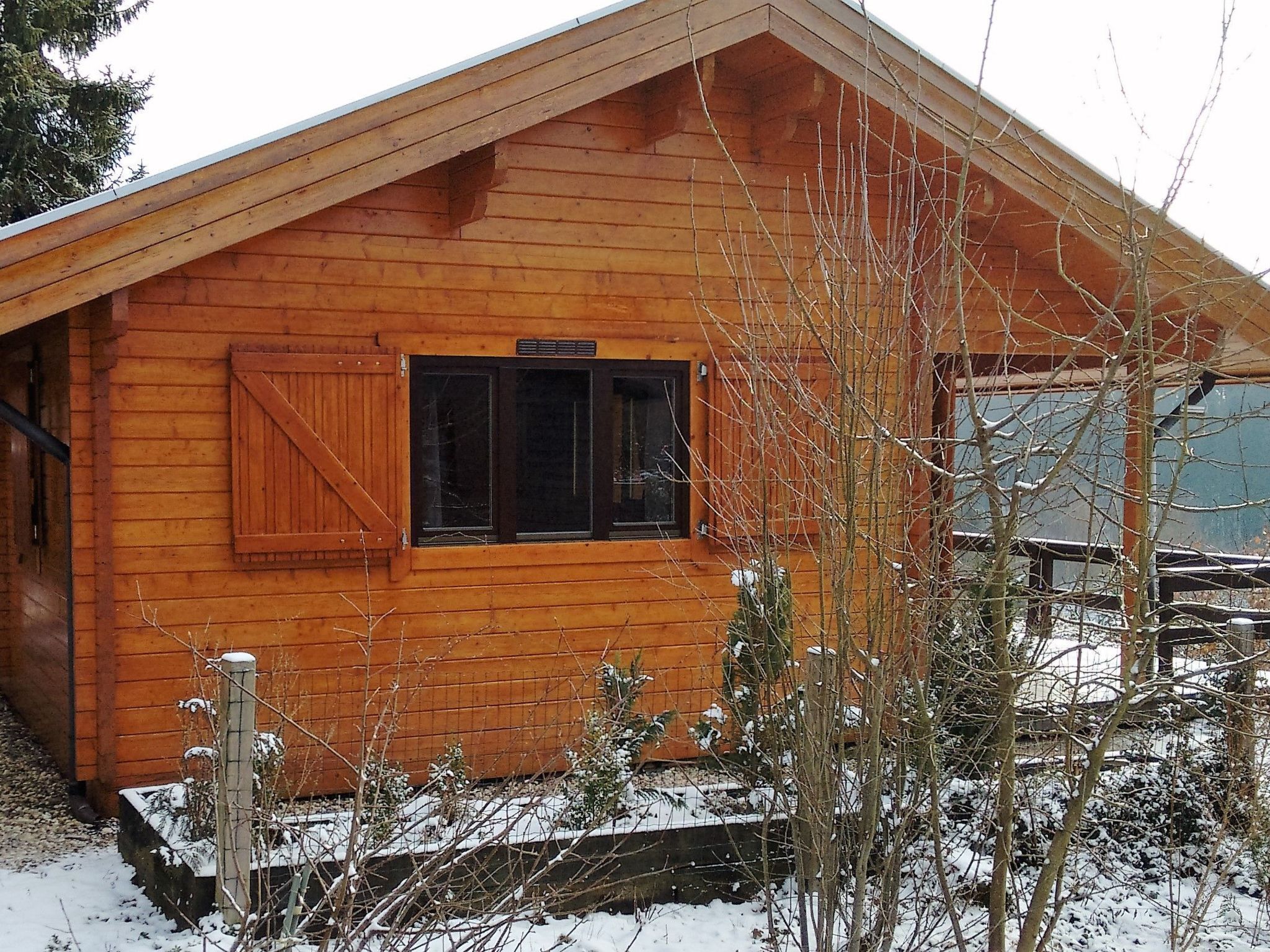 A wooden cabin with a gabled roof, a window with shutters, and a small porch area.