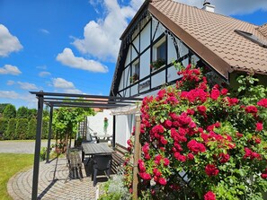 Ein traditionelles Fachwerkhäuschen mit Gartenlaube, Sitzgelegenheiten im Freien und einer Pergola.