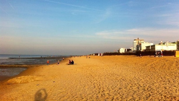 Ein weiter Sandstrand mit blauem Himmel und einigen Gebäuden im Hintergrund.