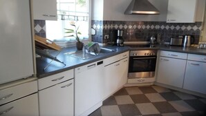 Eine moderne Küche mit weißen Schränken, einem Edelstahlherd, einer Kaffeemaschine und einem Fenster mit Pflanze.